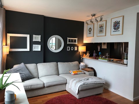 A living room with a grey couch and a round mirror on the wall.