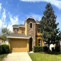 a yellow house with a driveway and a tree in front of it