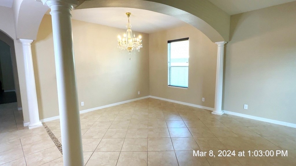 an empty dining room with pillars and a chandelier