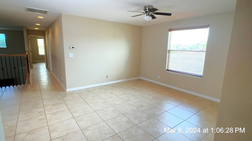 an empty living room with tile flooring and a ceiling fan