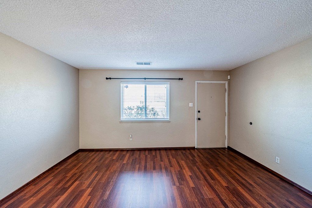 the living room of an empty house with wood floors and a window