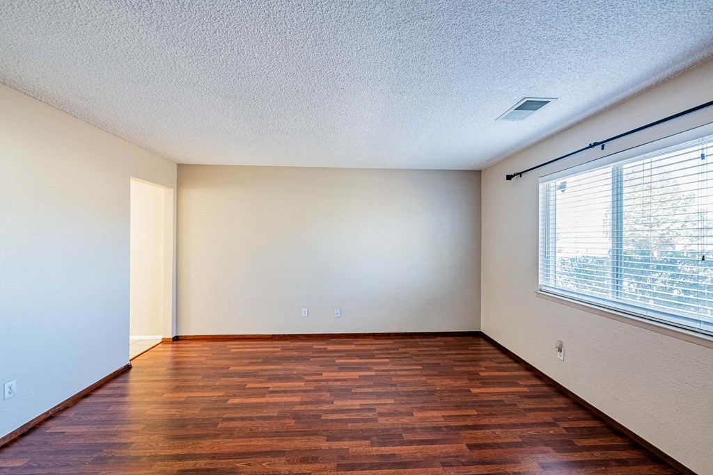 an empty living room with a large window and wooden floors