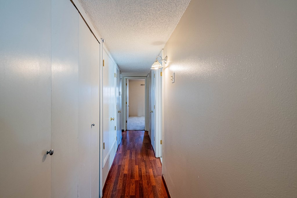 a hallway with wood flooring and white walls and a door to a bedroom