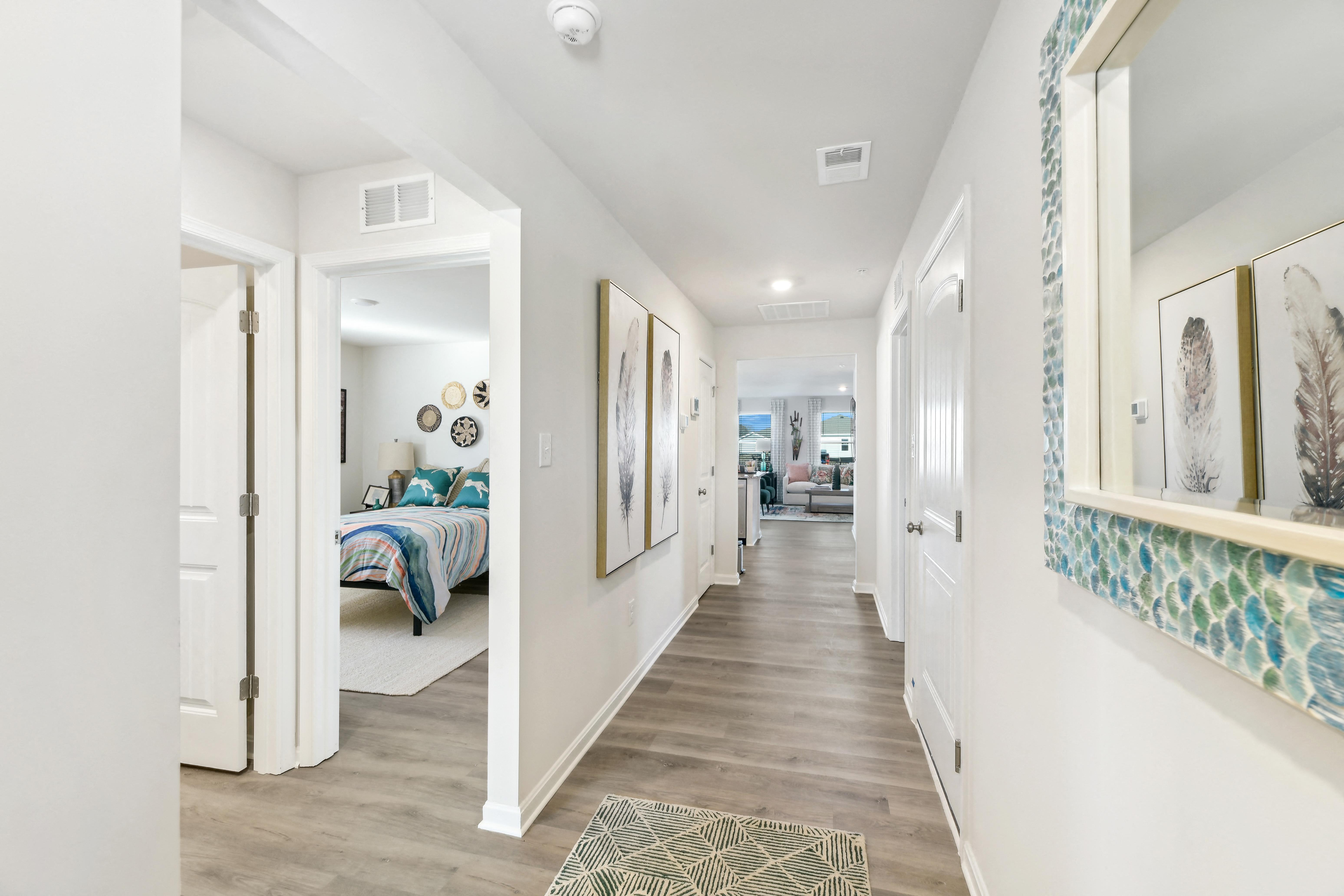 a long hallway with white walls and wood flooring and a bedroom with a bed
