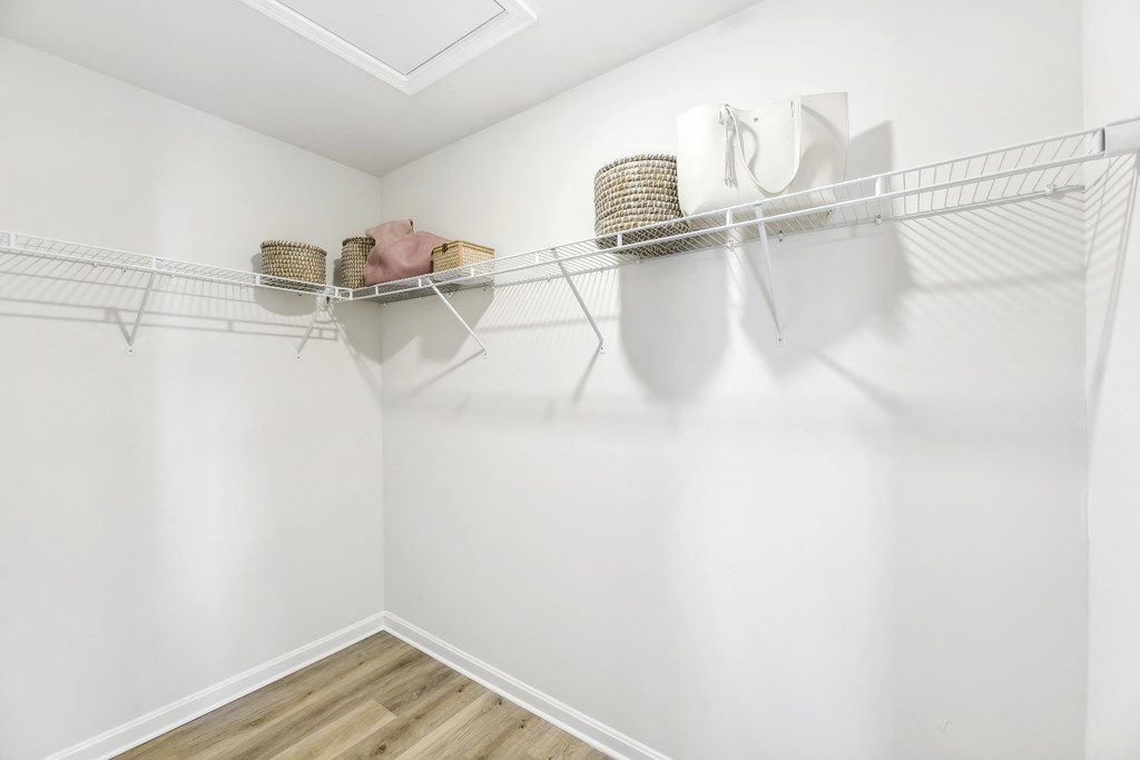 a spacious closet with white walls and shelves and a white walled closet with hooks