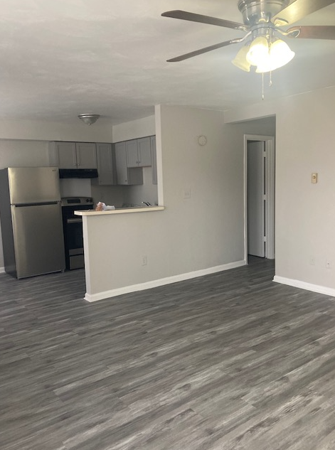 an empty living room with a kitchen and a ceiling fan