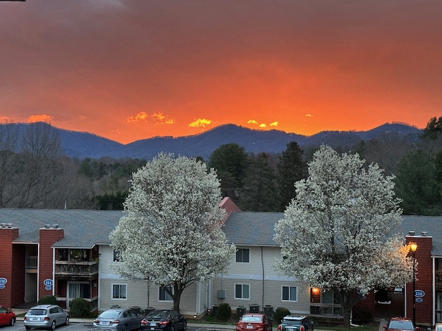 A sunset view of a mountain range with a building and trees in the foreground.