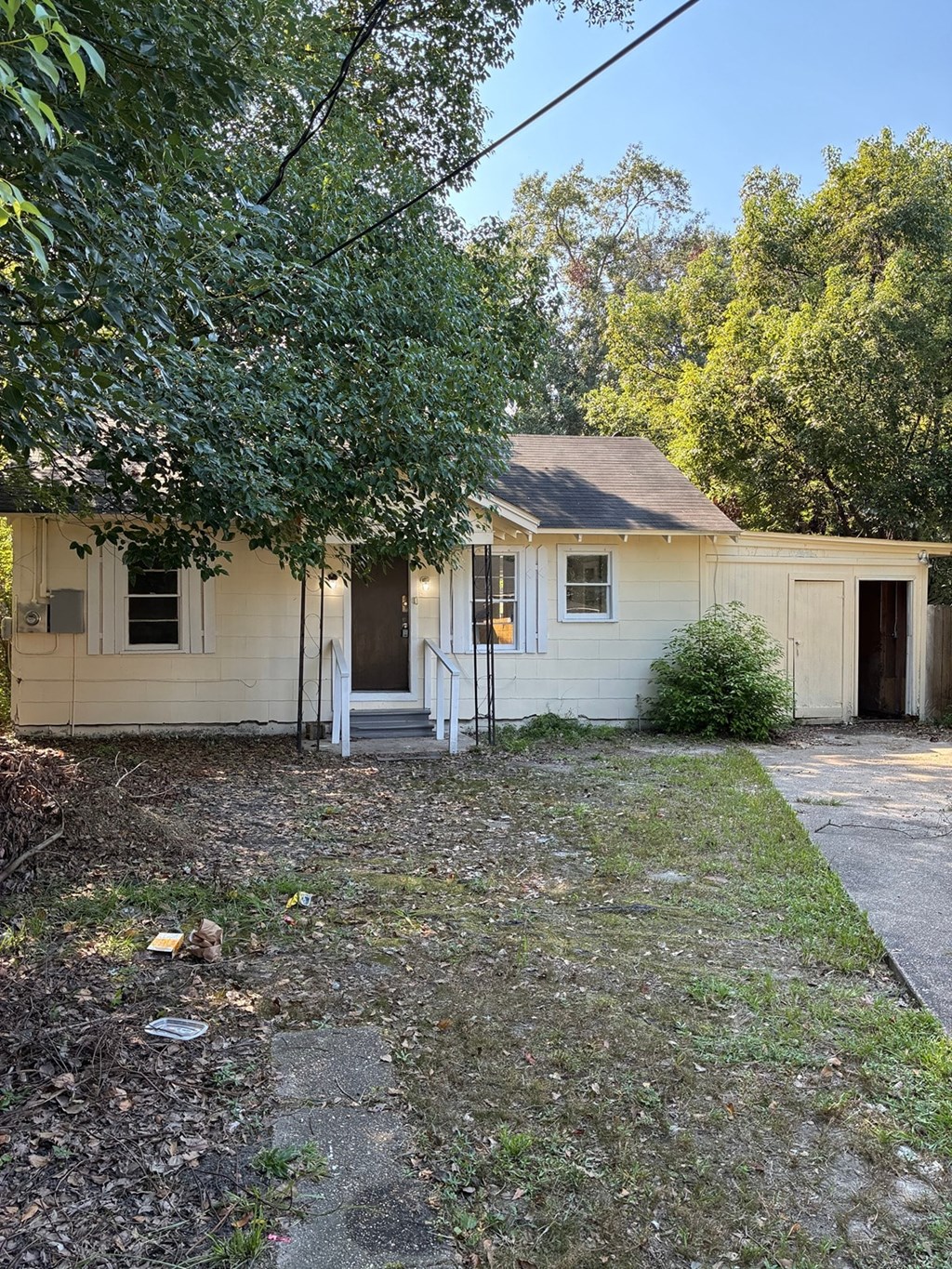 A small white house with a brown roof and a tree in front.