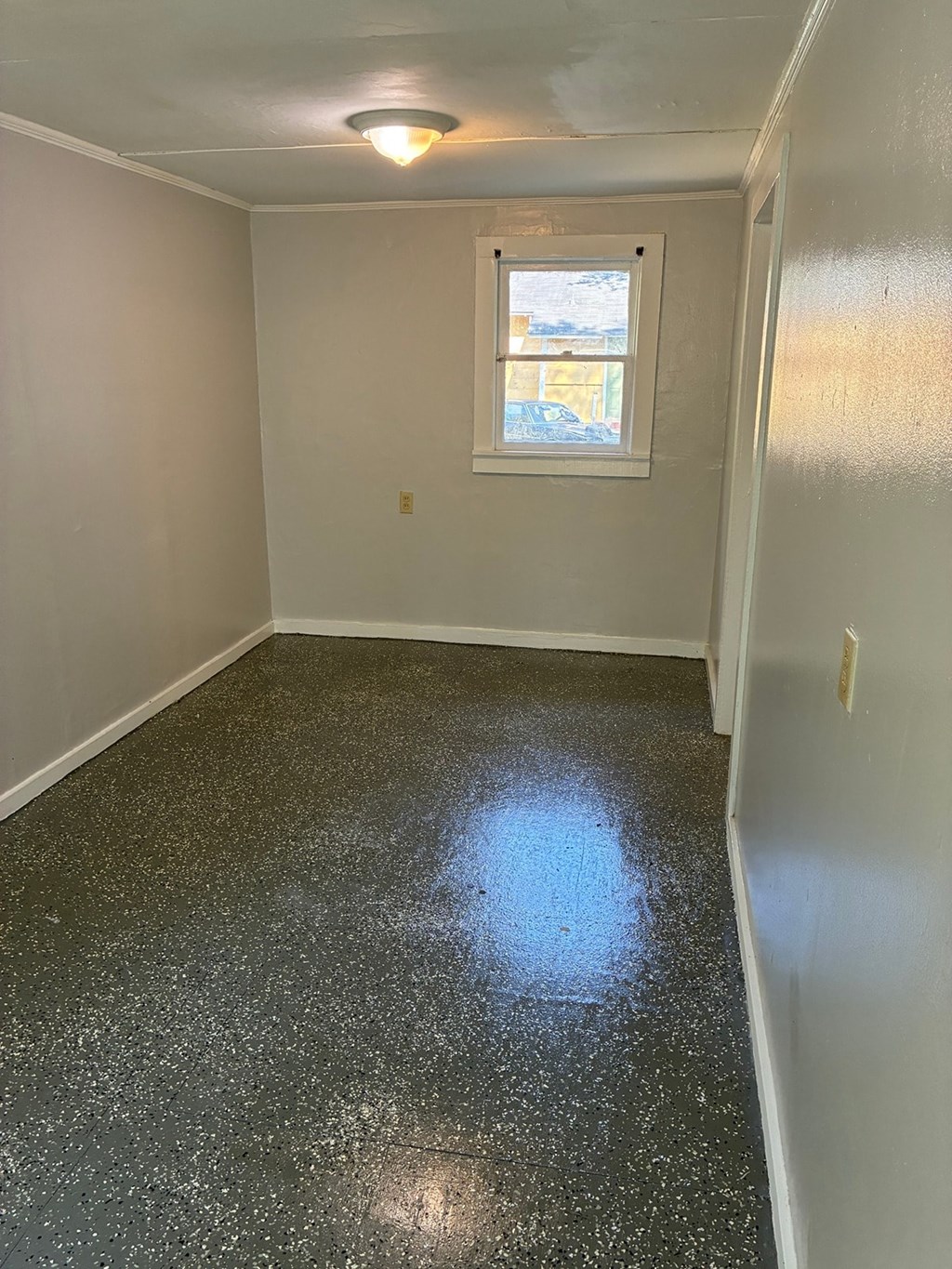A room with a window and a speckled floor.