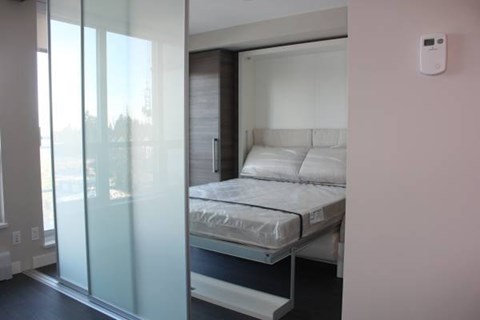 A bedroom with a bed, a window, and a white wall.