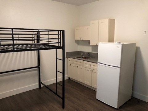 A white refrigerator sits in a kitchen next to a black bunk bed.