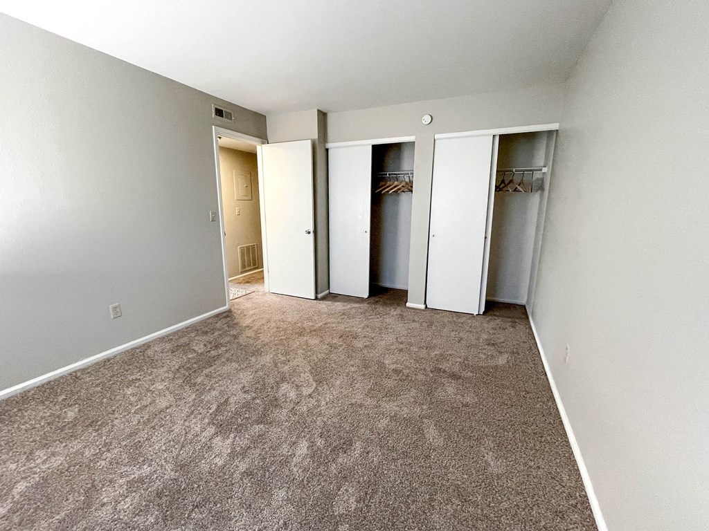 an empty room with carpet and doors to three closets