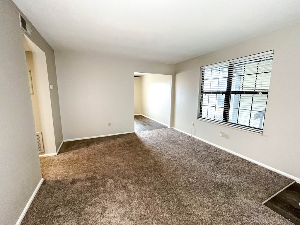 an empty living room with a large window and carpeting