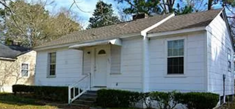 A small white house with a porch and a front yard.