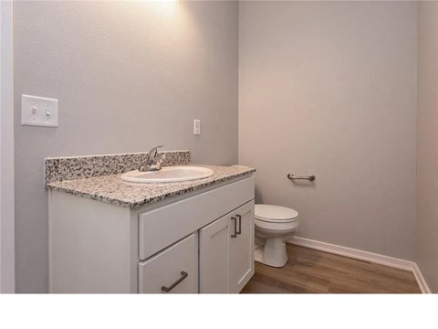 A bathroom with a sink, toilet, and wooden floor.