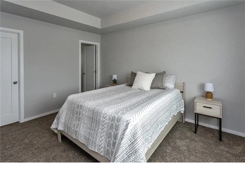 A bedroom with a bed, nightstand, and carpeted floor.