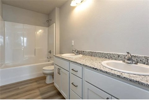 A white bathroom with a marble countertop and a white toilet.