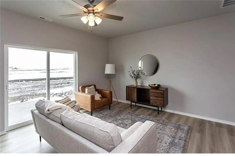A living room with a grey sofa, a wooden cabinet, a round mirror, and a ceiling fan.