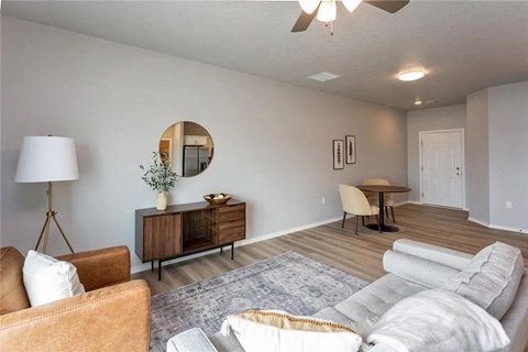 A living room with a brown chair, a grey sofa, a wooden cabinet, a round mirror, and a ceiling fan.