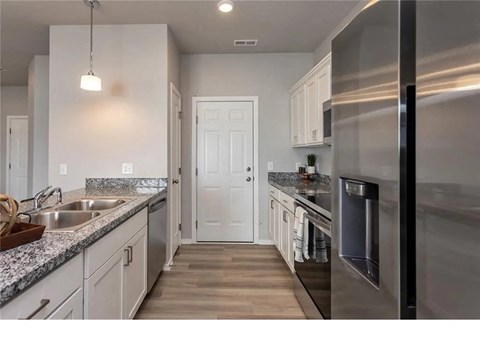A modern kitchen with a stainless steel refrigerator and wooden flooring.