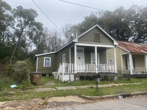 A house with a porch and a trash can in front of it.