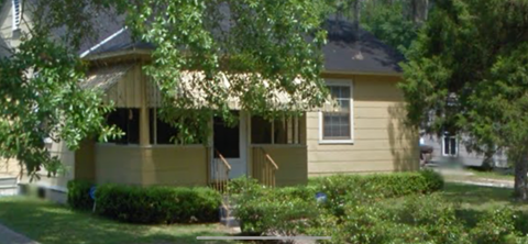 A yellow house with a porch and a tree in front.