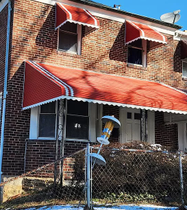 an old brick house with an orange awning and a sign in front