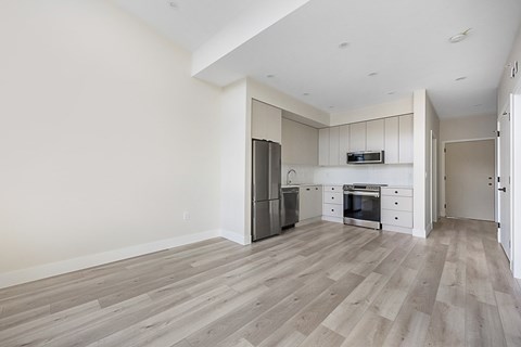 an empty living room with white walls and a kitchen with stainless steel appliances