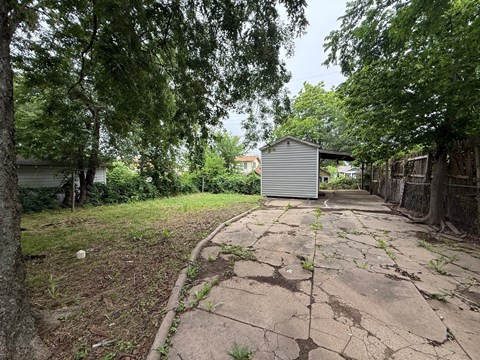 A cracked concrete pathway leads to a small building in a backyard.