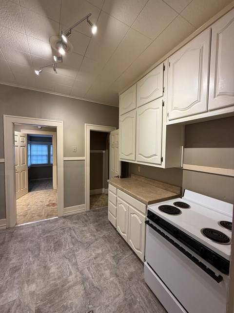 A kitchen with white cabinets and a white stove top oven.