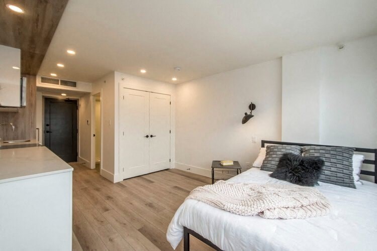 a white bedroom with a bed and a kitchen