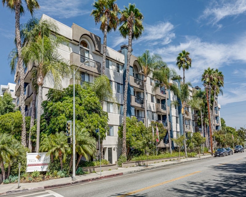 an apartment building with palm trees on the side of a street