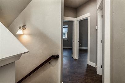 a hallway with a staircase and a white wall with a lamp