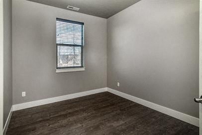 an empty bedroom with a window and wooden floors