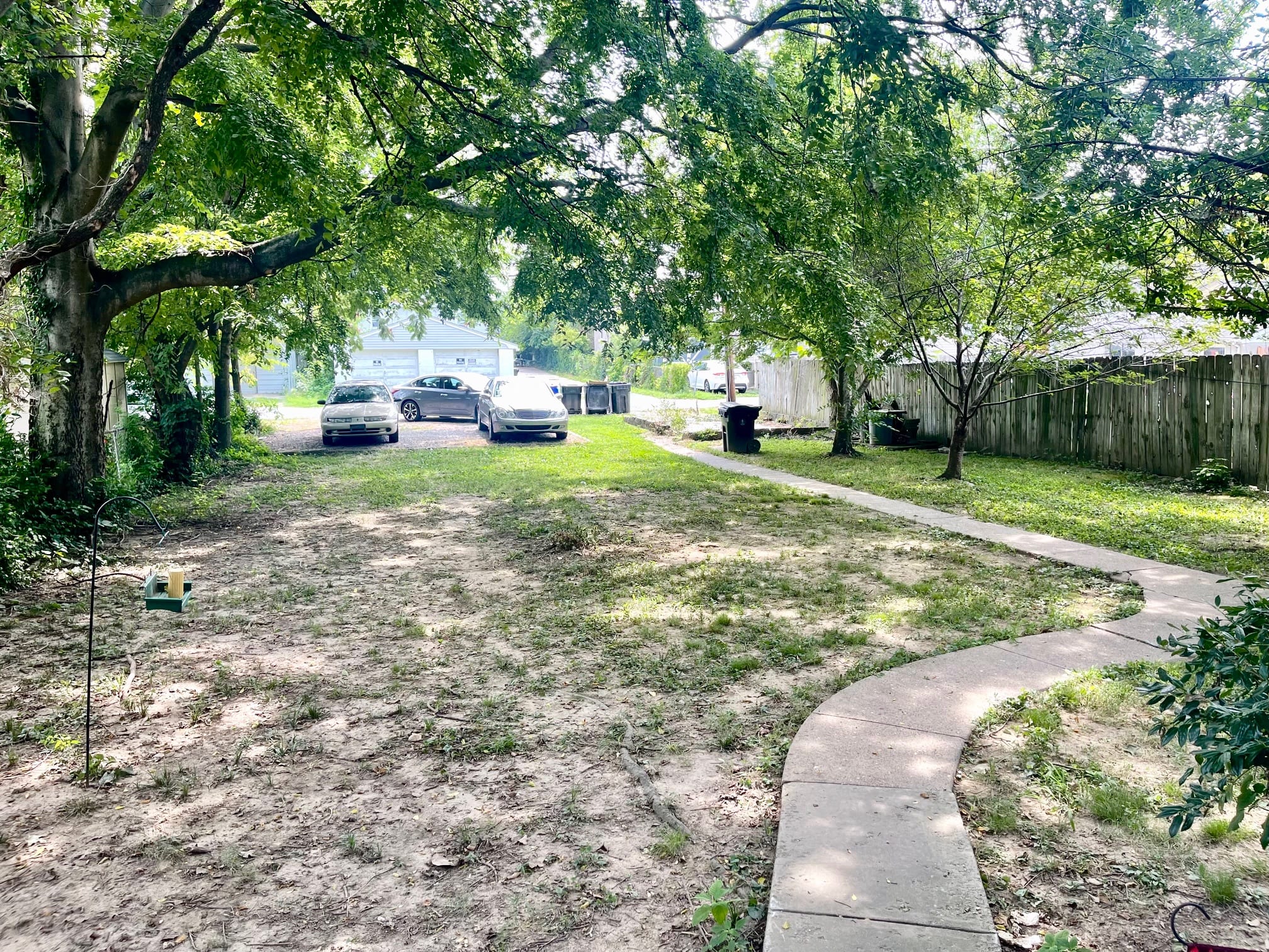 a sidewalk running through a yard with cars parked on the street