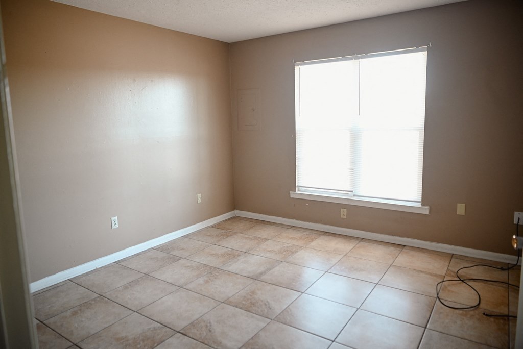 an empty living room with a window and tiled floors