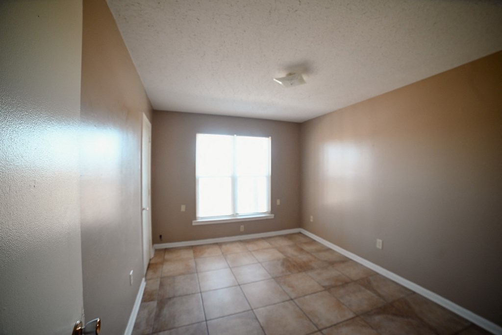 an empty living room with a window and tiled floors