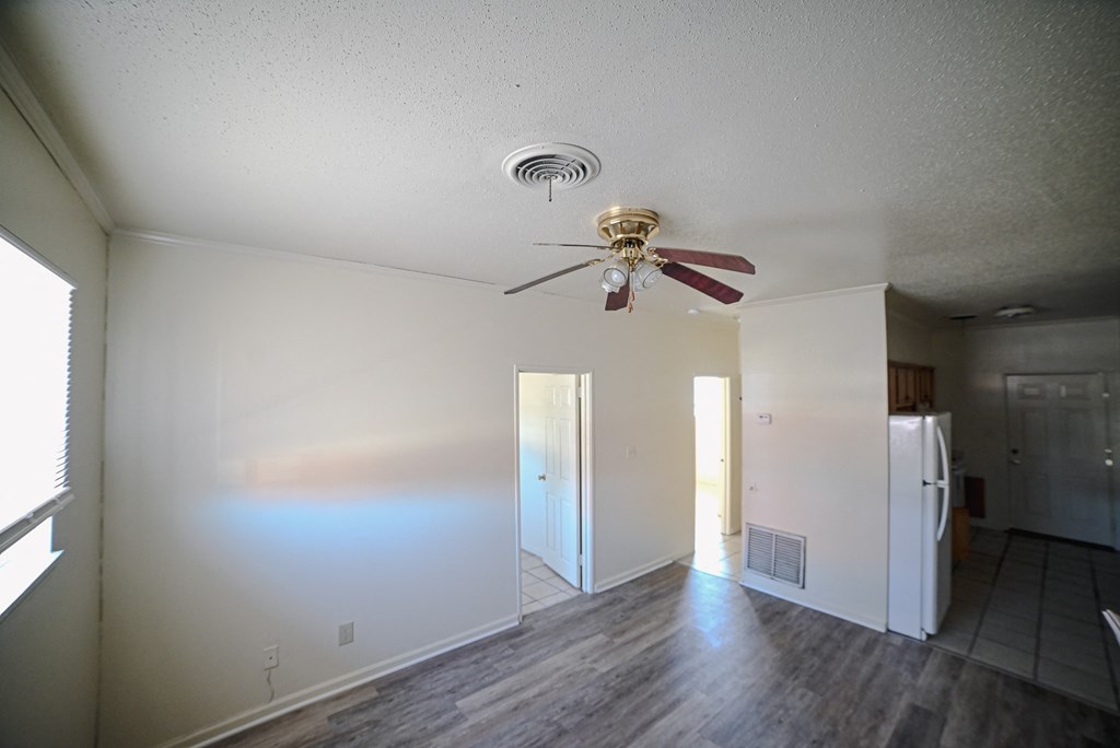 an empty living room with a ceiling fan and a kitchen