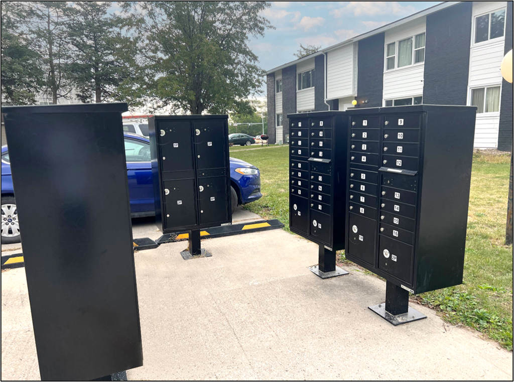 a group of mailboxes in front of a building with a blue car
