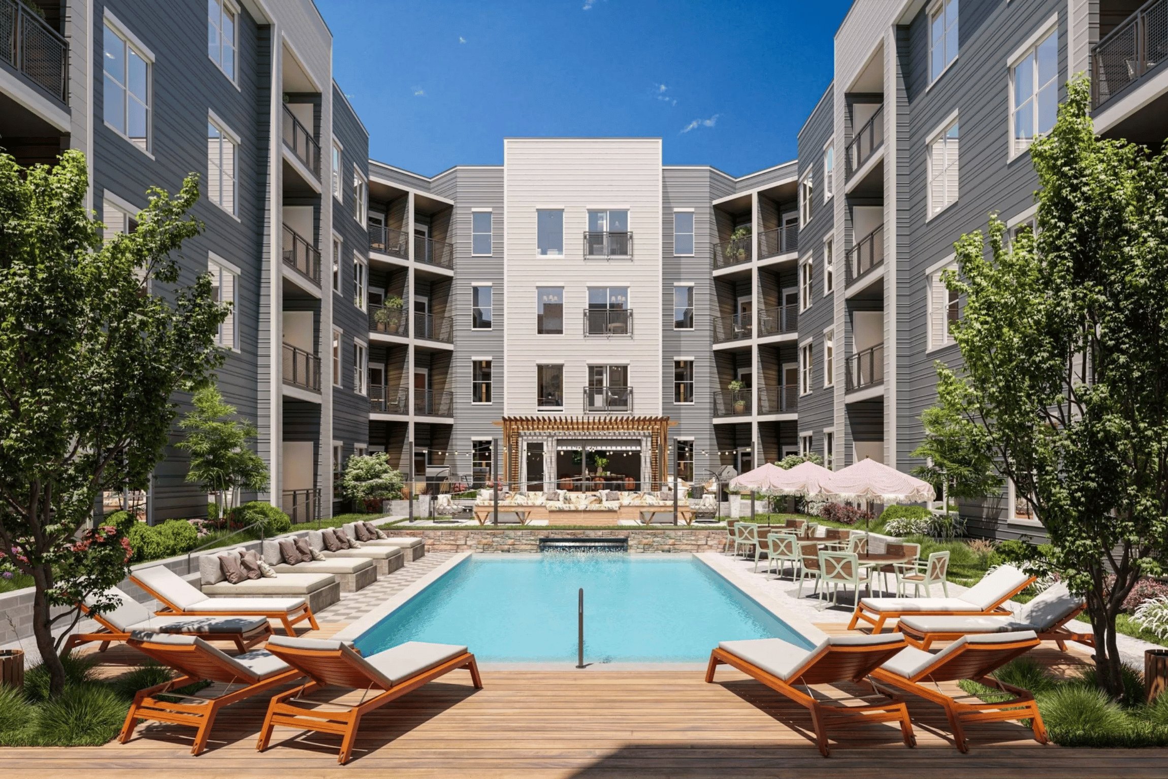 A large swimming pool surrounded by wooden deck chairs and lounge umbrellas in front of a modern apartment complex.
