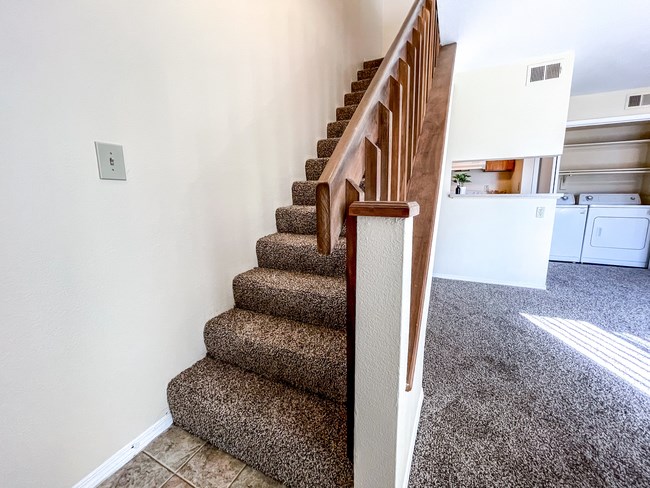 an image of a carpeted staircase in a home with white walls and a railing