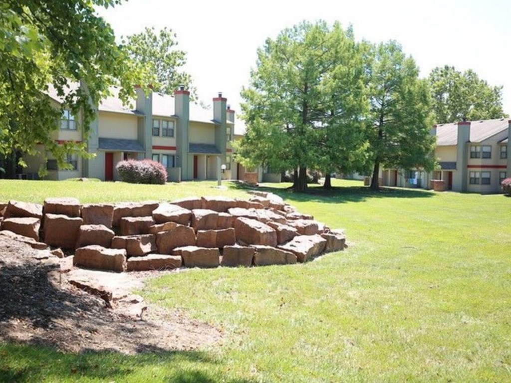 a stone retaining wall in the grass in front of an apartment building