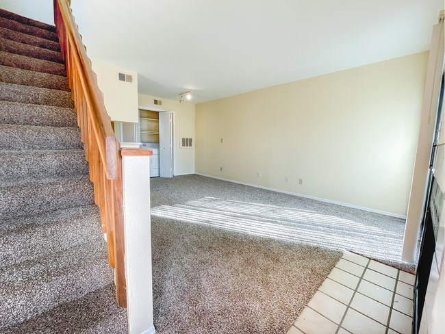 an empty living room with stairs and a carpeted floor