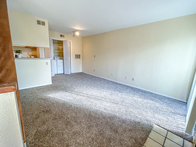 an empty living room with carpet and a kitchen