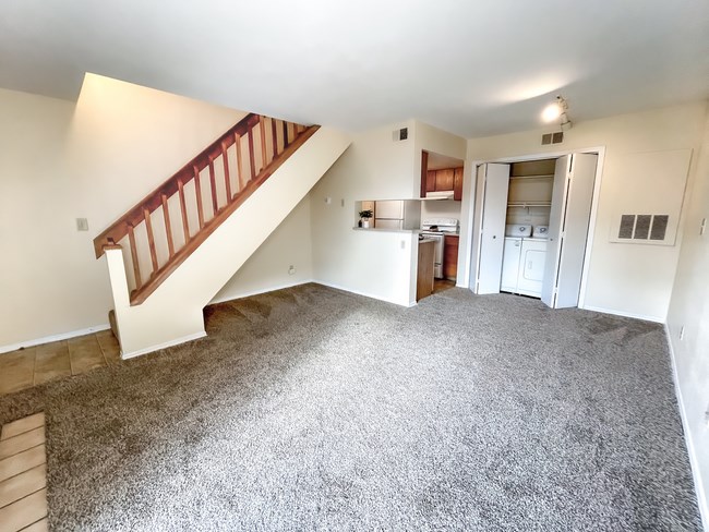 an empty living room with a staircase and a kitchen