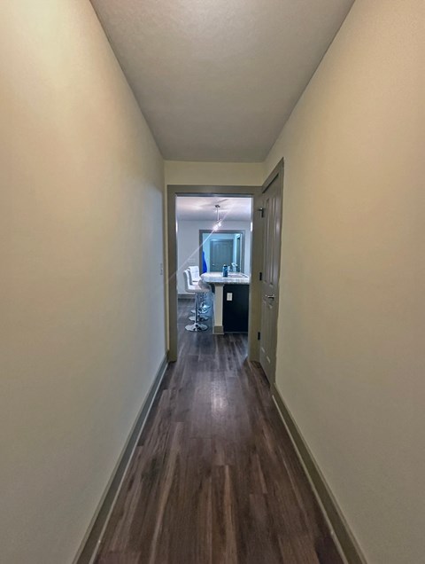 a long hallway with wood floors and white walls and a kitchen in the distance
