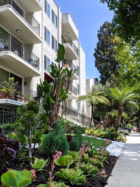 A white apartment building with a balcony and a garden in front.