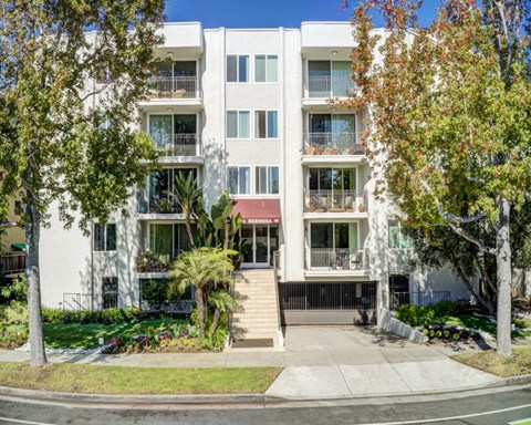 A white apartment building with a red awning and trees in front.