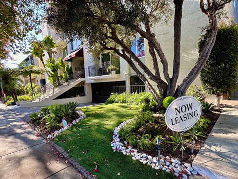 A "Now Leasing" sign is in front of a landscaped area and a building.
