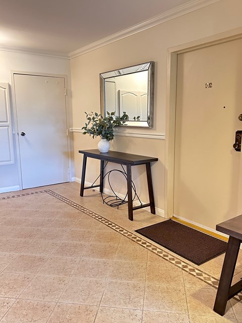 A hallway with a table and chairs and a mirror on the wall.